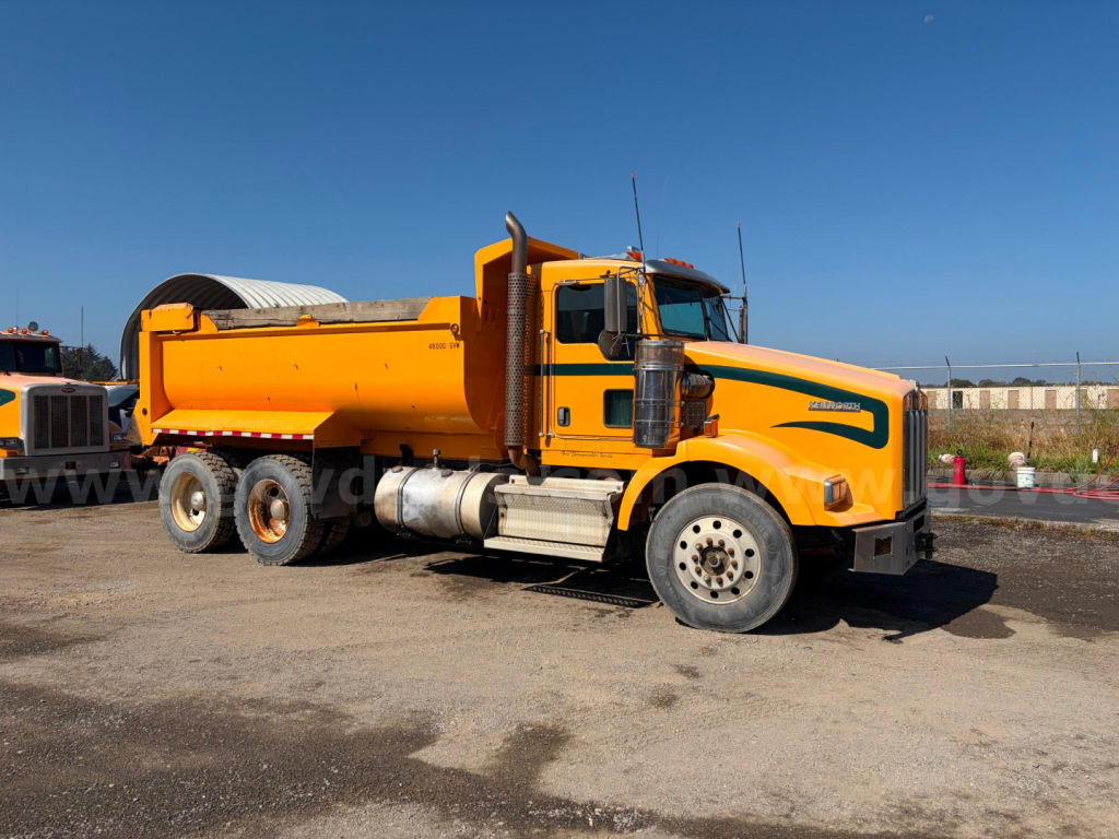 Kenworth T800B dump truck in orange with front cab and rear dump bed, side view showing fuel tanks and dual rear axles.