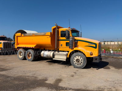 Kenworth T800B dump truck in orange with front cab and rear dump bed, side view showing fuel tanks and dual rear axles.