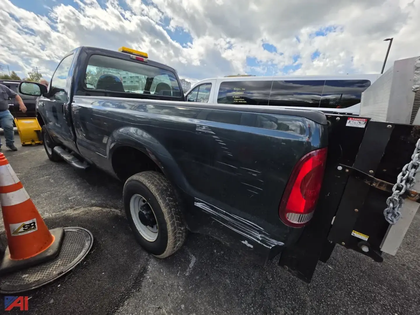Ford F-250 Super Duty pickup with plow and liftgate side view showing damage on passenger side bed and wheels on asphalt.