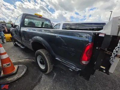 Ford F-250 Super Duty pickup with plow and liftgate side view showing damage on passenger side bed and wheels on asphalt.