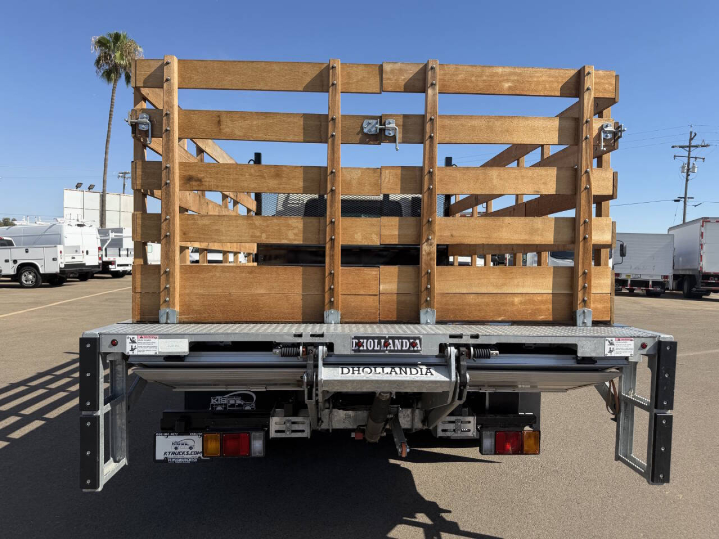 Flatbed truck rear showing wooden stake bed and Hollandia hydraulic tailgate, with bumper and lights visible.