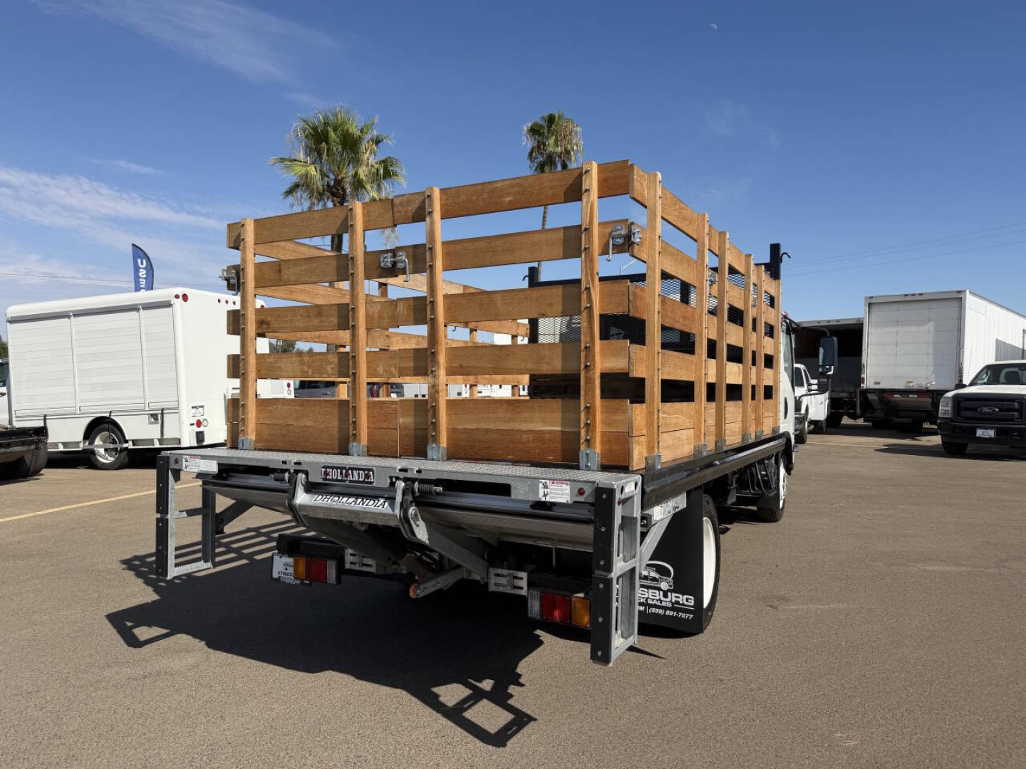 Chevrolet 4500 flatbed truck with wooden stake sides and rear-view showing stock number 7906 at a dealership yard.