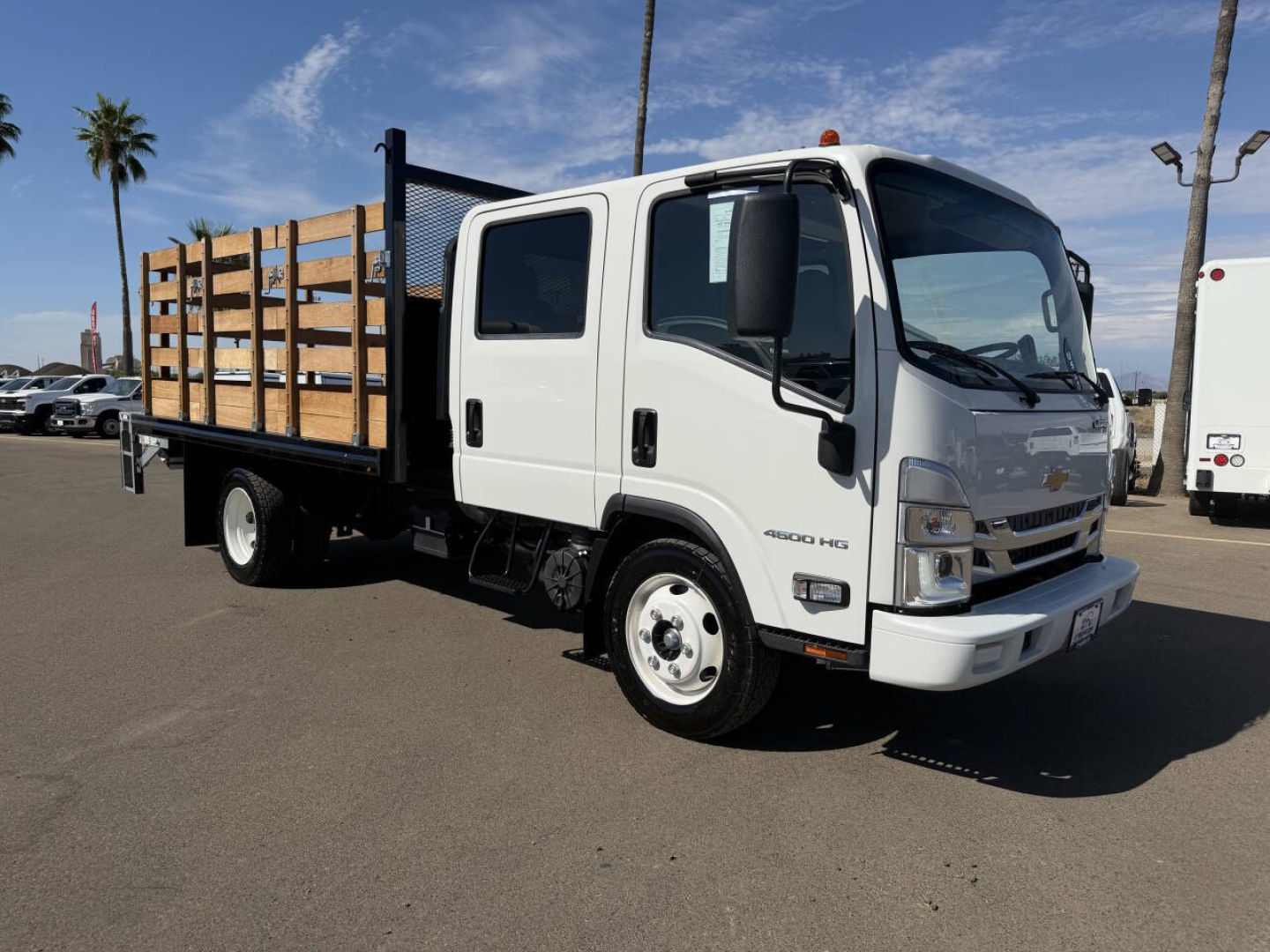 Flatbed truck showing Chevrolet 4500 HD label and wood-sided flatbed with metal rails, white cab, side mirror, and dual rear wheels.