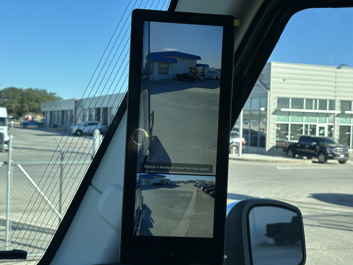 Truck cab interior mirror displaying exterior lot with dealership buildings and other vehicles.