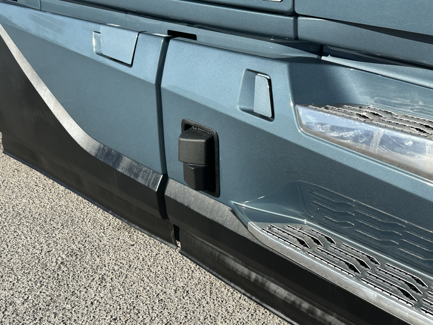 Front bumper area of a Volvo VNL64T860 truck showing a black rectangular tow/connector cover and chrome side steps.