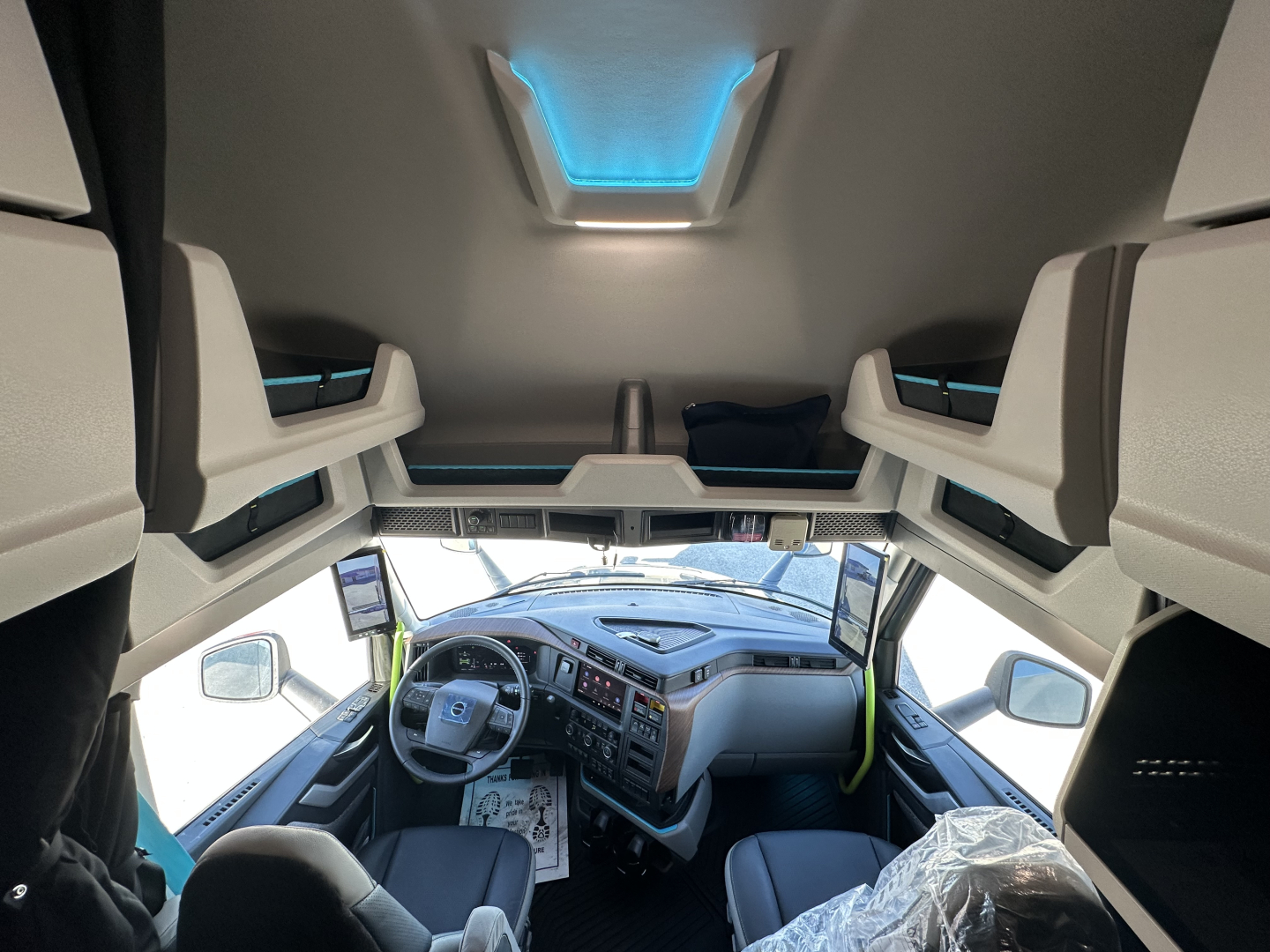 Interior view of a 2026 Volvo VNL64T860 sleeper cab showing steering wheel, dashboard, and overhead storage with blue accent lighting.