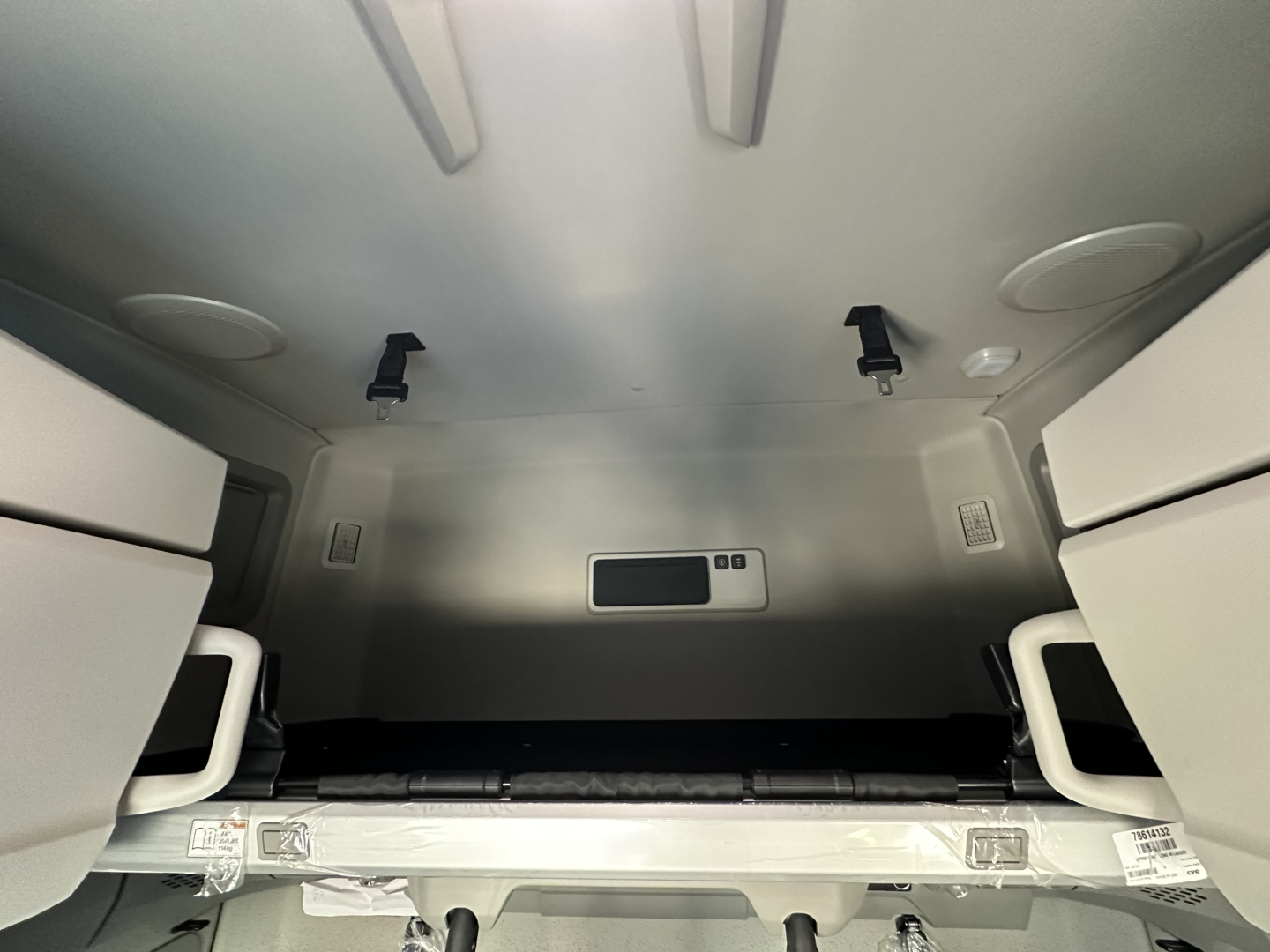  Volvo VNL64T860 sleeper cab interior storage area with overhead shelves and tie-downs, rear-view image shows metallic interior walls and a small rectangular cabinet.