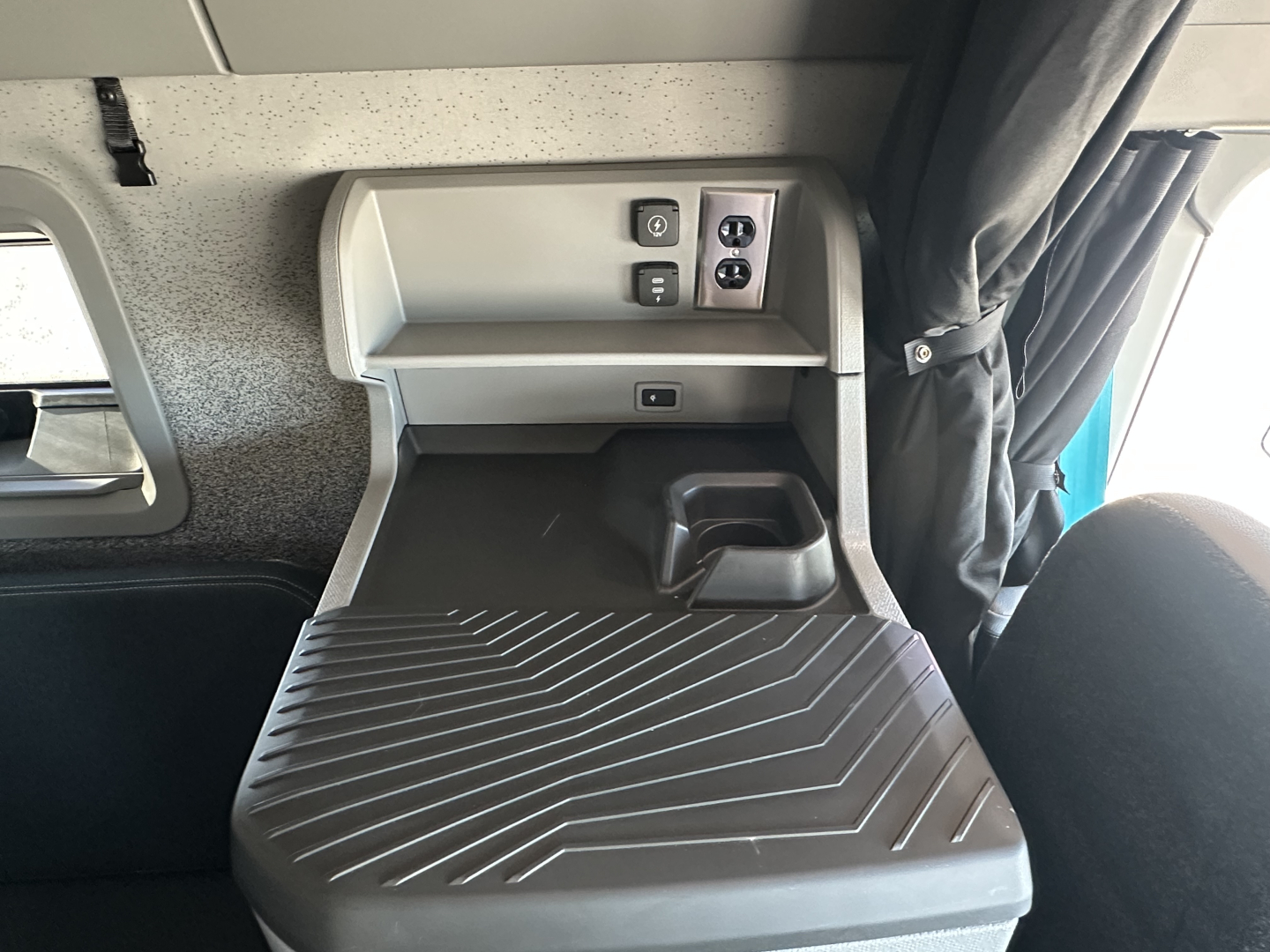 Volvo VNL64T860 sleeper cab interior showing dashboard controls and storage shelf with ribbed floor mat.