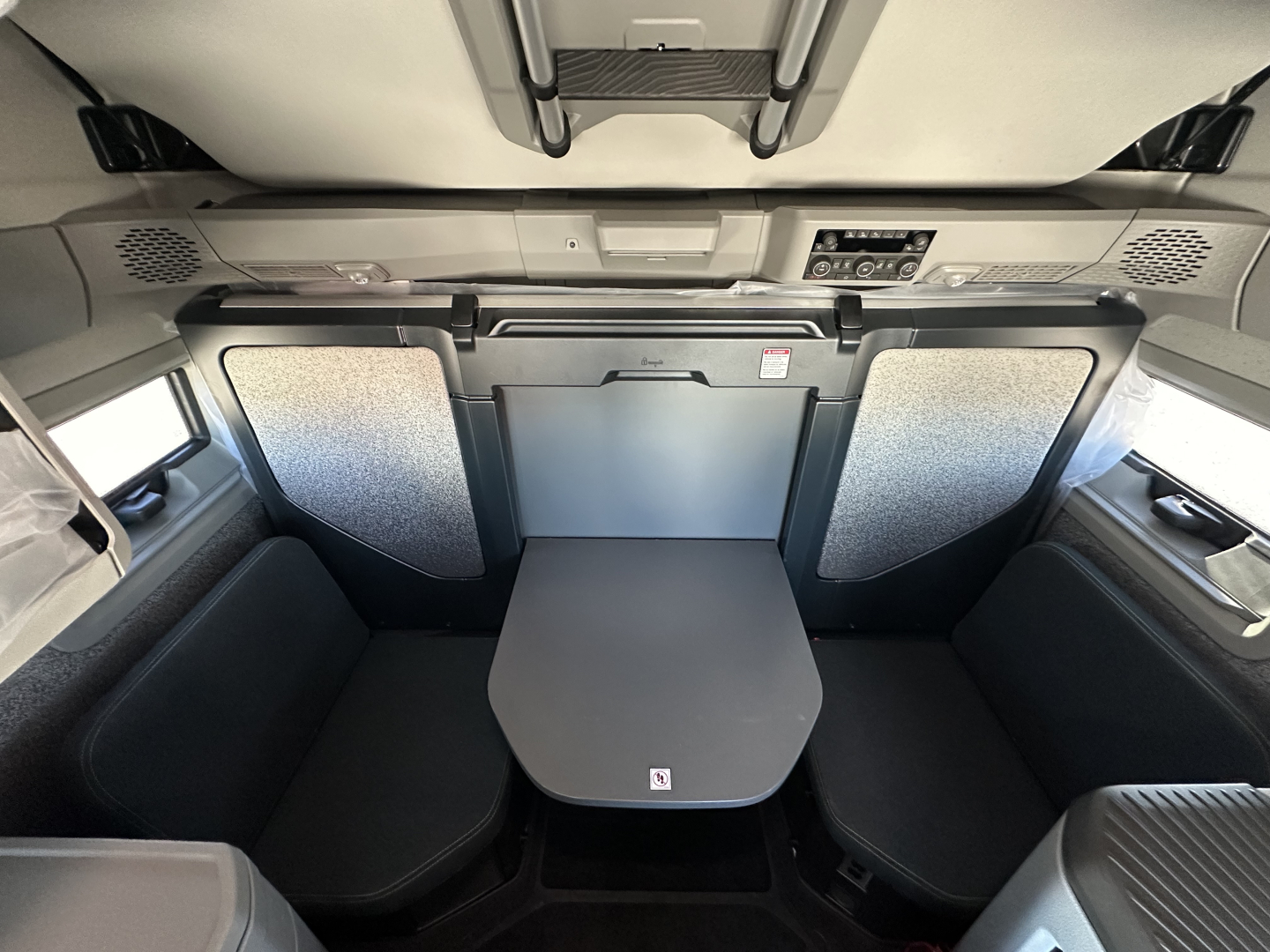 Interior sleeper cab of a Volvo truck with a central table and seating panels. controls and overhead storage visible along with side panels.