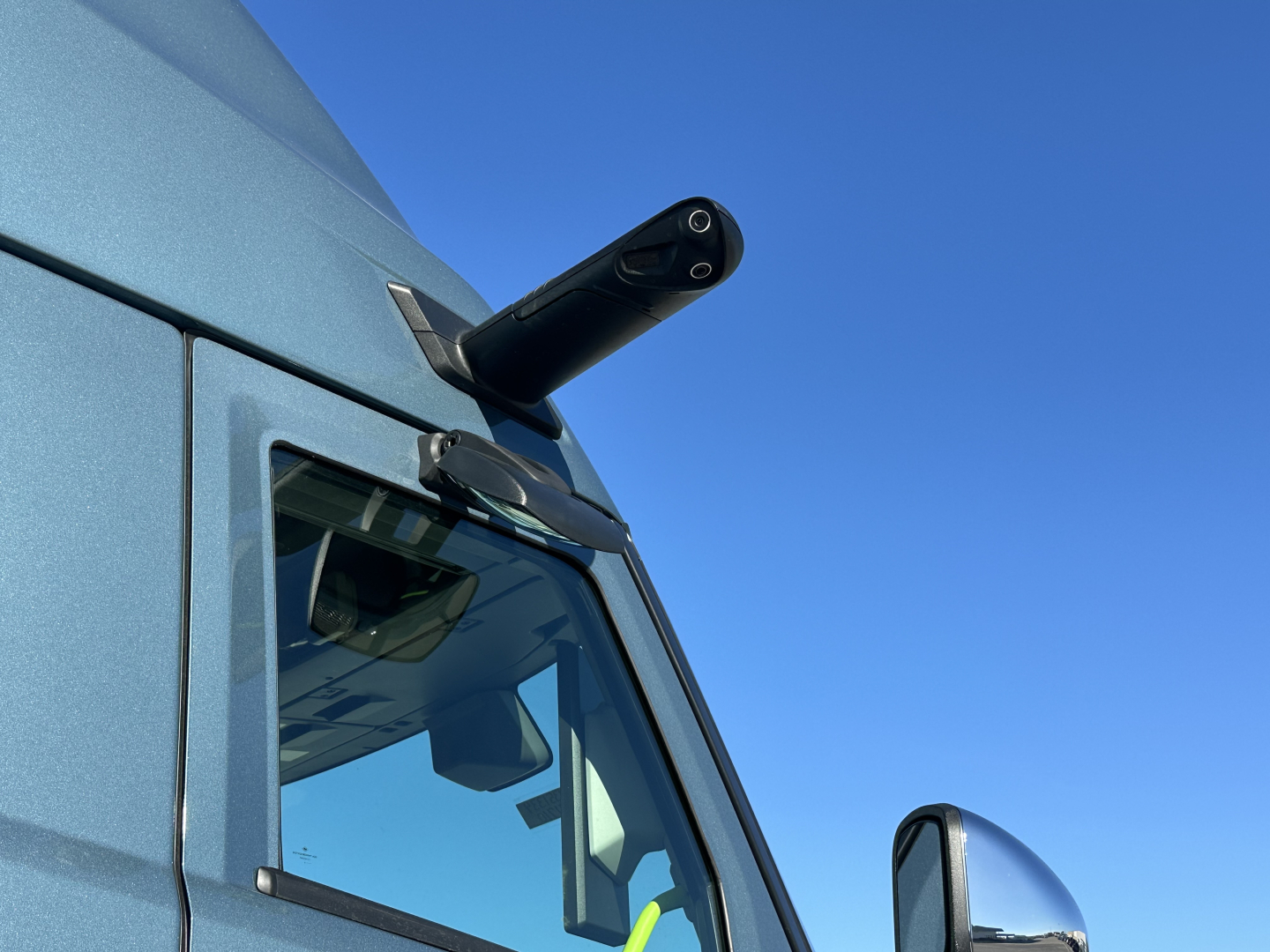 Volvo VNL truck corner view showing side mirror and window, blue sky.