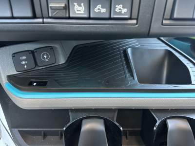 Volvo VNL64T860 interior center console area showing USB/12V port cover and ambient blue trim; dashboard control buttons visible above with various indicators.