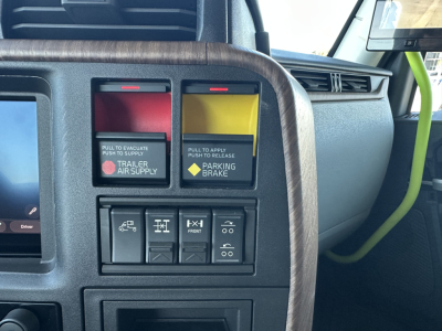 Volvo truck interior panel with emergency red/amber switches and labeled controls, woodgrain trim, center display, and yellow/black warning buttons.