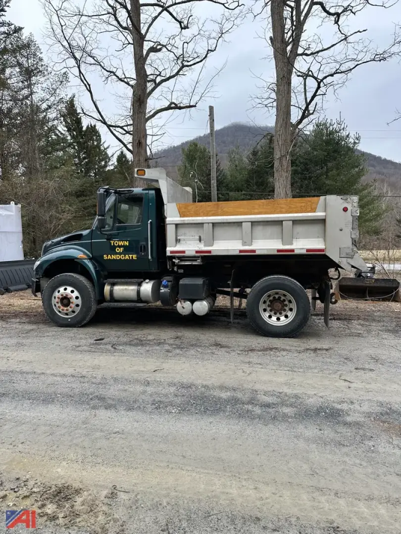 Dump truck side view showing 2018 International 4400SBA with green cab and white dump bed; text on door reads Town of Sandgate.