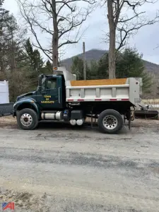Dump truck side view showing 2018 International 4400SBA with green cab and white dump bed; text on door reads Town of Sandgate.