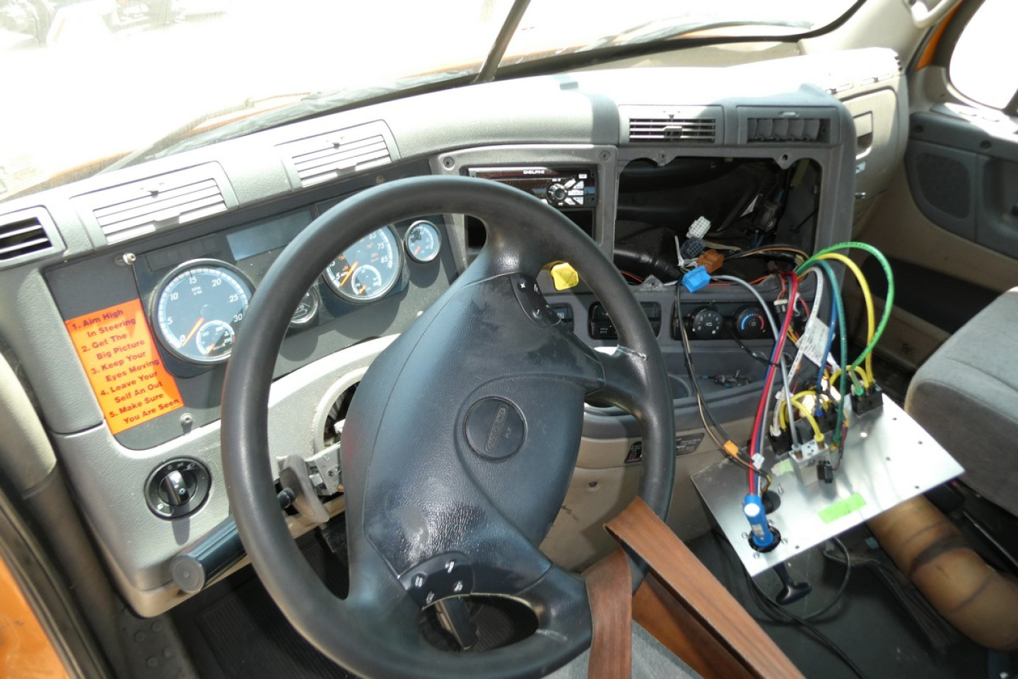 Cab interior of a Freightliner Cascadia 125 truck showing steering wheel, gauge cluster, exposed electrical wiring, and dashboard components.