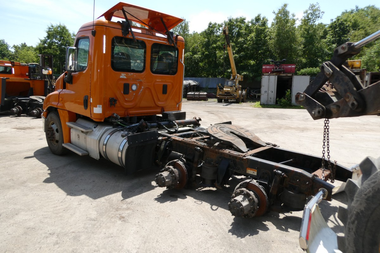 Orange 2016 Freightliner Cascadia 125 daycab tractor chassis with exposed drive axles and missing trailer, side view showing cab and rear drivetrain components.
