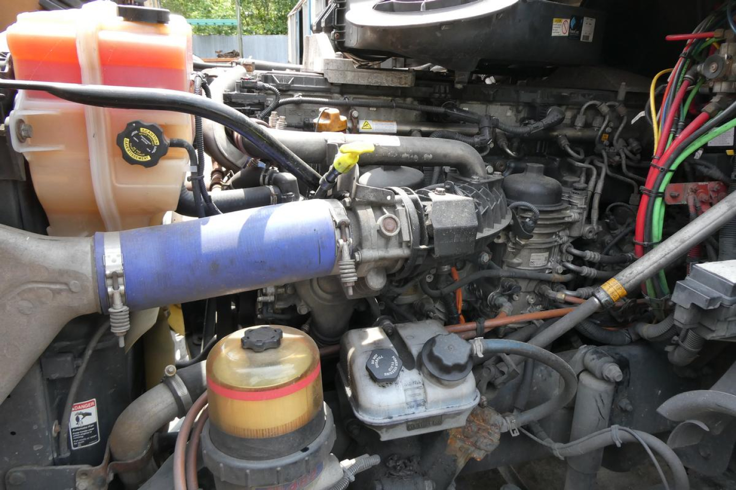 Truck engine bay showing coolant reservoir, power steering fluid reservoir caps, hoses, and various engine components.
