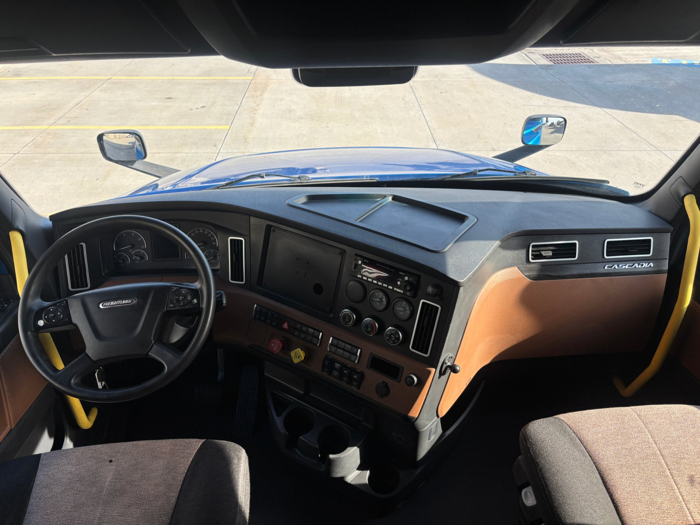 Truck cab interior of a Freightliner PT126064ST sleeper, dashboard and steering wheel visible, with tan and black panels and control panels.