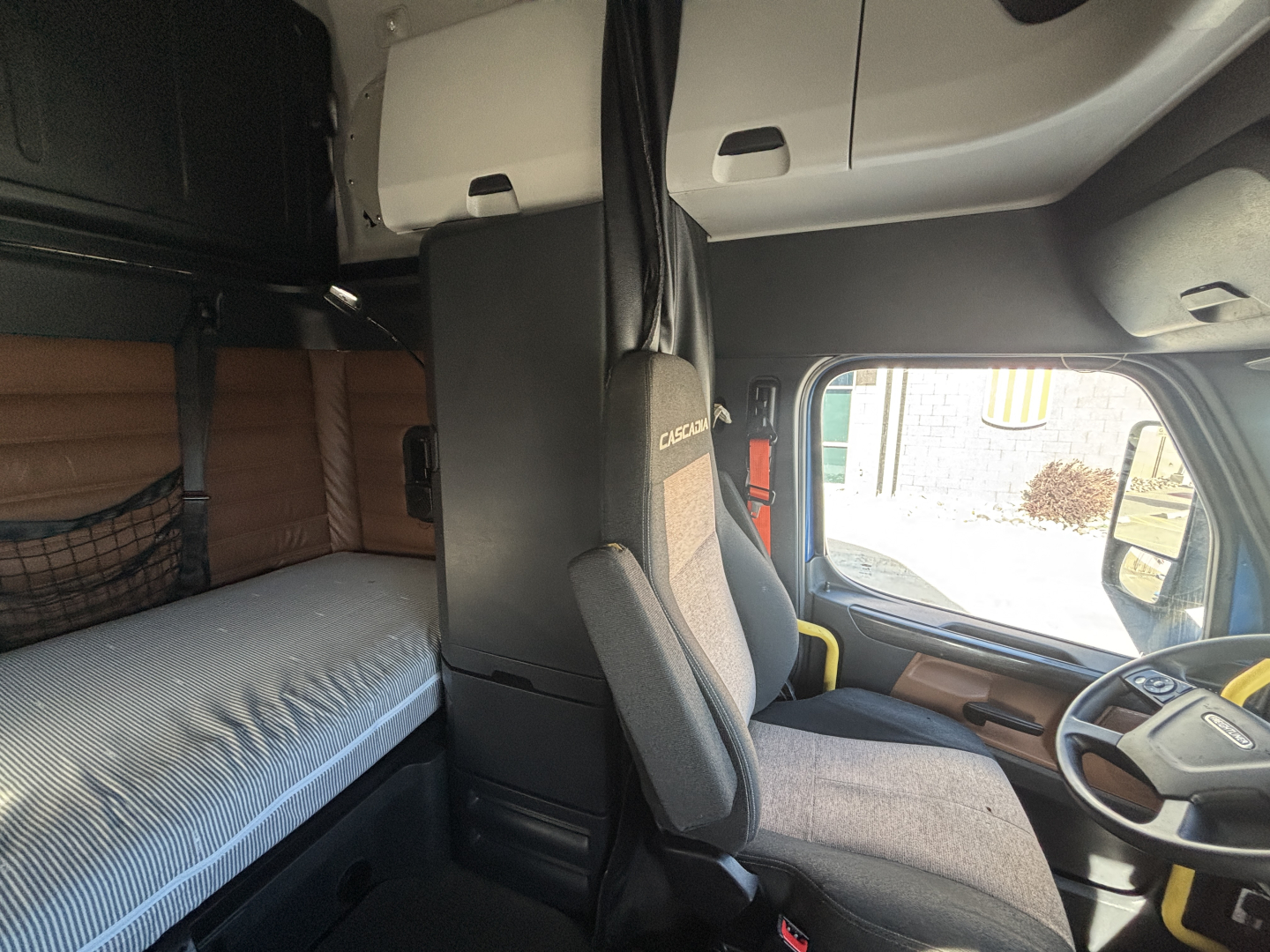 Cab interior of a Freightliner truck showing driver seat and sleeper berth with bunk area and dashboard details visible.