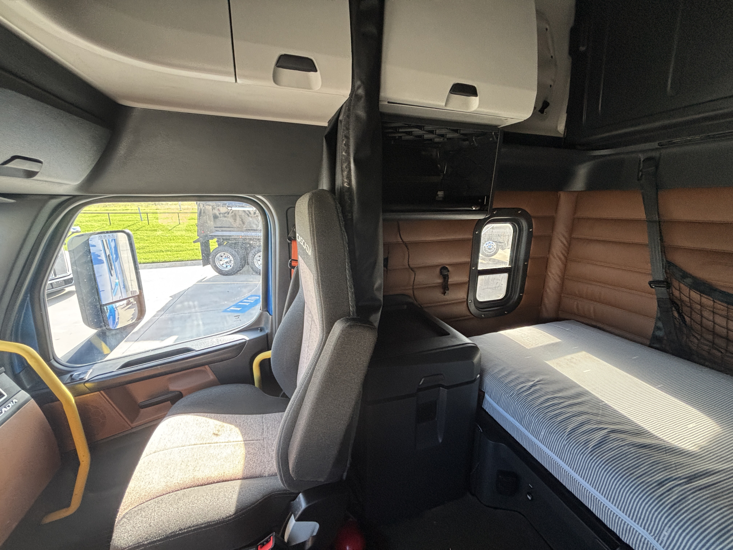 Truck cab interior view from left side showing sleeper berth with window and storage compartments.