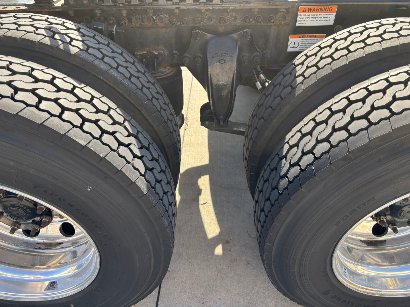 Truck rear dual tires and suspension components visible under the frame of a Freightliner tractor trailer.