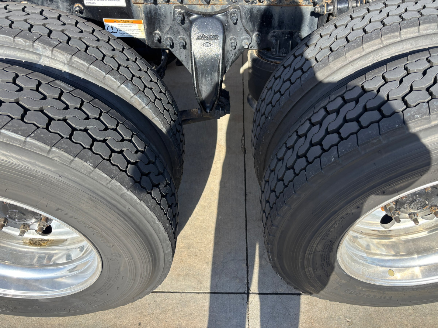 Two large rear dual tires of a Freightliner truck with suspension assembly between them; visible tire treads and metal wheel rims.