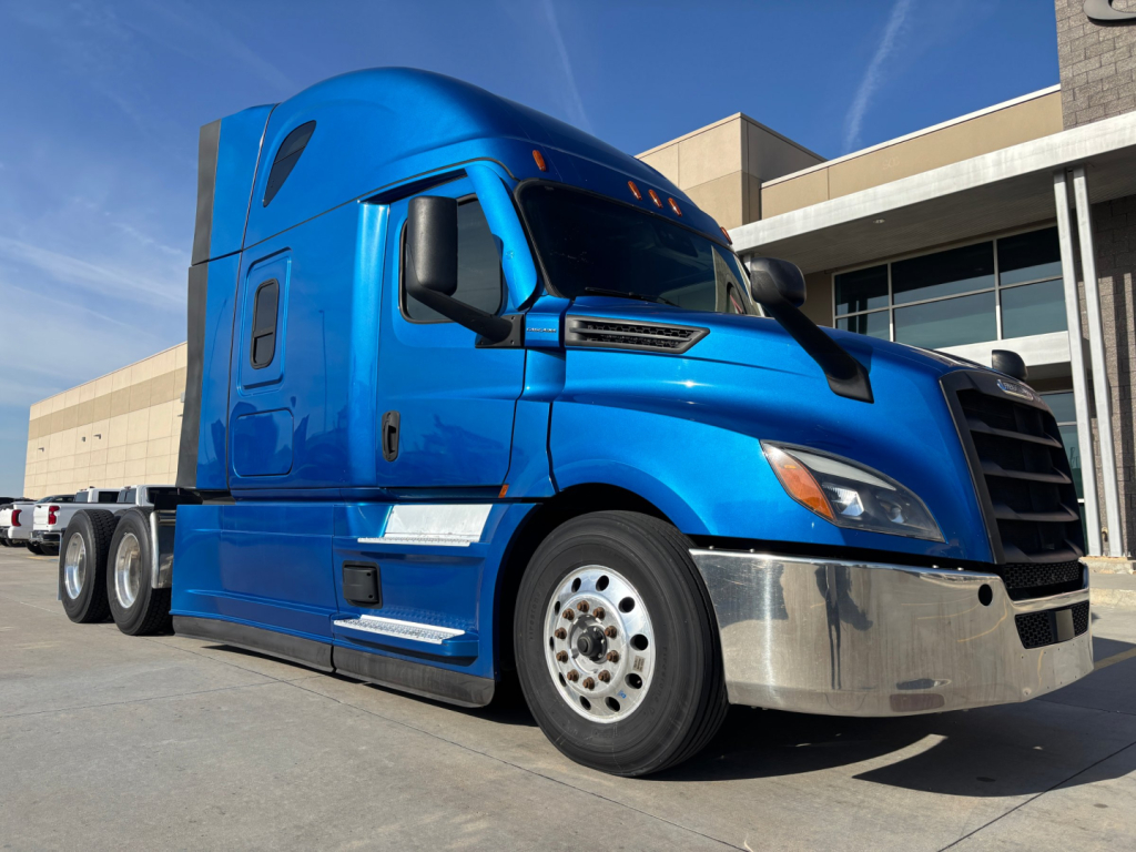 Truck cab and front of blue Freightliner PT126064ST tractor with chrome bumper and black grille showing wheel and side mirror details.