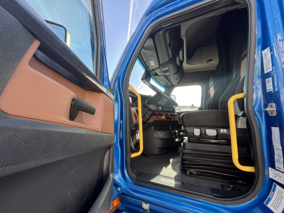 Truck cab interior door open showing driver seat and dashboard of a blue Freightliner PT126064ST conventional sleeper.