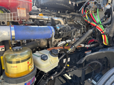 Trucks engine bay with wiring harnesses and blue intercooler hose; coolant reservoir, power steering/washer fluid reservoirs, and various hoses visible.