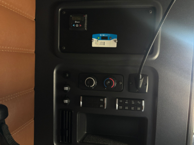 Cab interior panel of a used Freightliner PT126064ST showing control panel with climate knobs, stereo-style switches, and a blue/white label on a device mounted in the upper cavity.