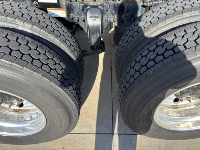 Two large rear dual tires of a Freightliner truck with suspension assembly between them; visible tire treads and metal wheel rims.