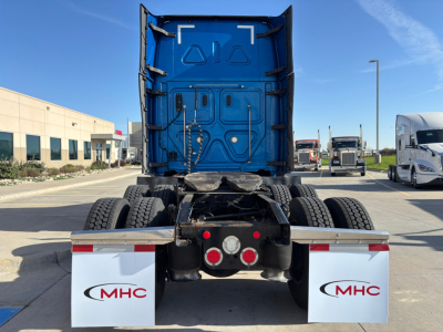 Rear view of a Freightliner truck tractor chassis showing dual rear axles and blue back of cab with MHC mud flaps.