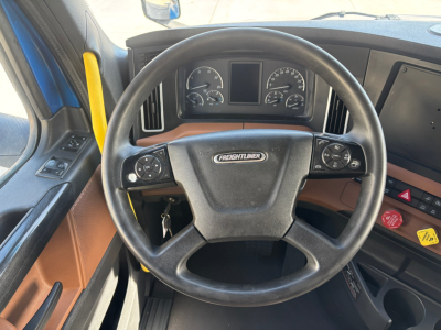 Steering wheel and dashboard of Freightliner PT126064ST semi truck cab; center shows Freightliner badge, gauge cluster and control panels on both sides.
