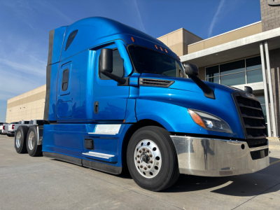 Truck cab and front of blue Freightliner PT126064ST tractor with chrome bumper and black grille showing wheel and side mirror details.