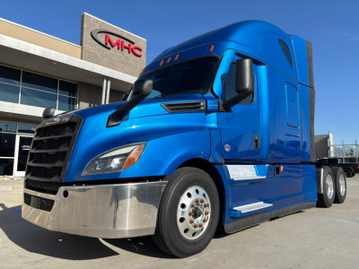 Freightliner semi truck in blue exterior parked outside dealership showing chrome front bumper and aerodynamic sleeper cab.