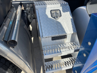 Aluminum diamond-plate toolbox and steps on a Freightliner truck undercarriage, with metal storage box and perforated steps.