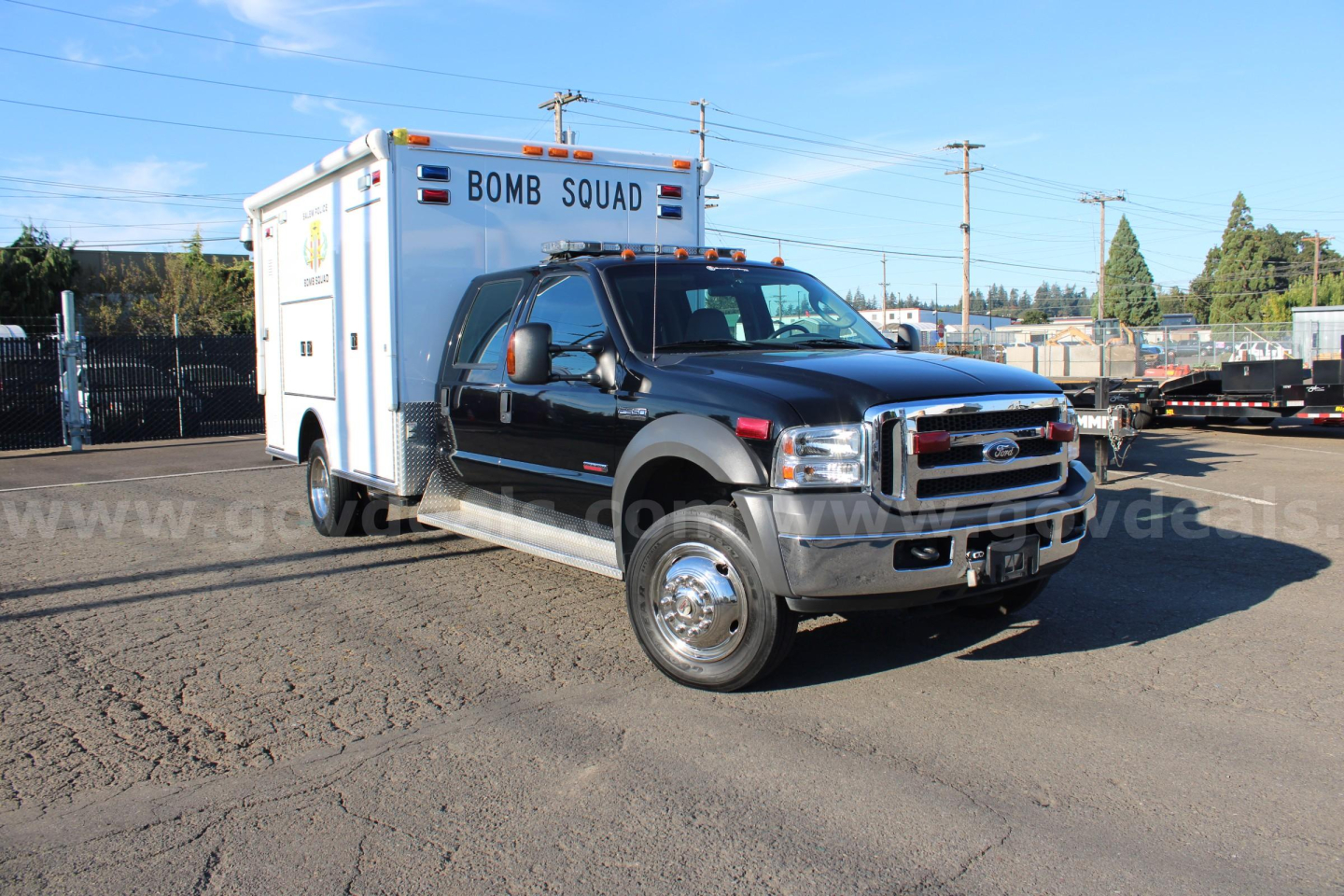 Ford F-550 cab and chassis with external box labeled BOMB SQUAD, black pickup, daytime outdoor lot.