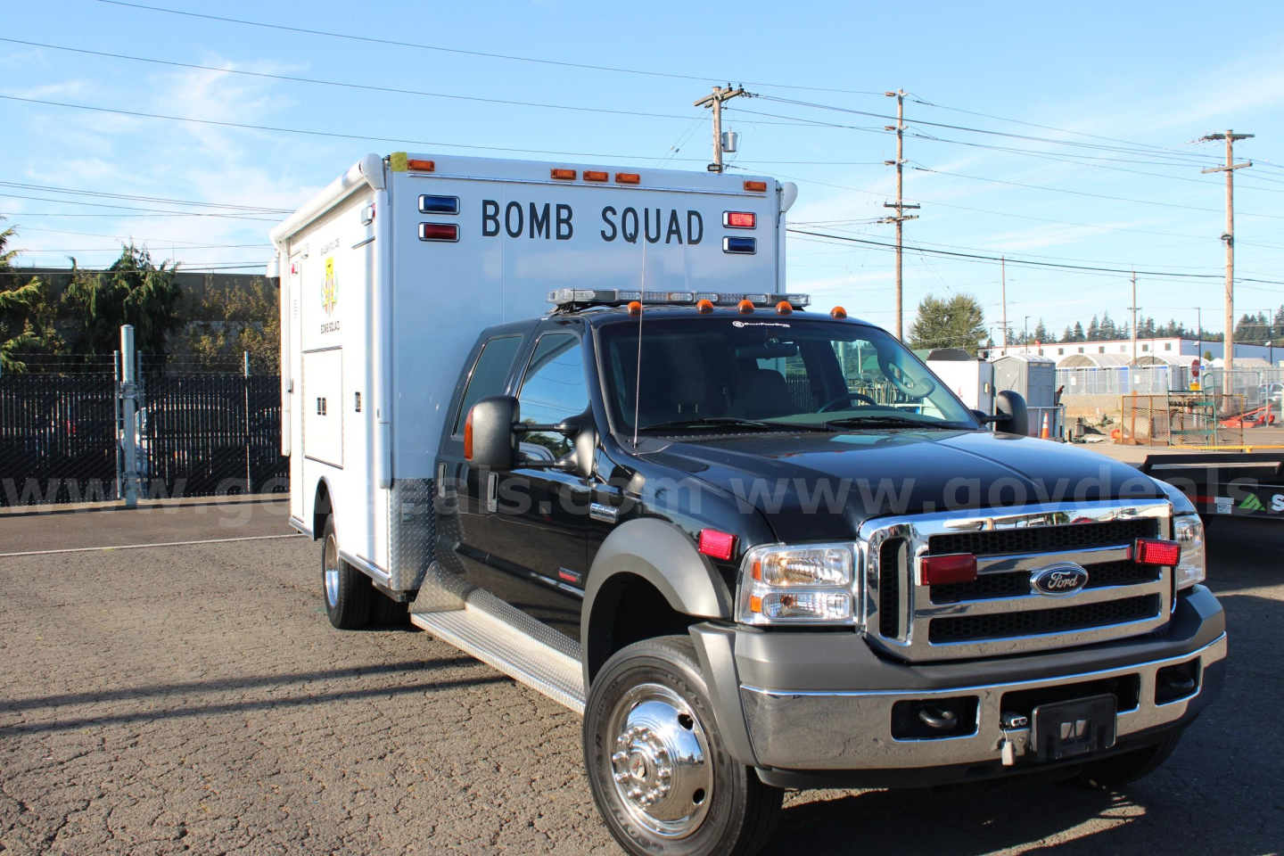 Ford F-550 cab and chassis with a rear Bomb Squad emergency box, front grille, and chrome wheels visible in a dealership lot.