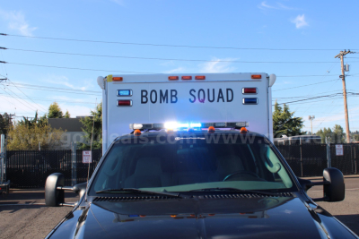 Back of a Ford F-550 cab and chassis with emergency light bar on top; text on the rear door reads BOMB SQUAD.