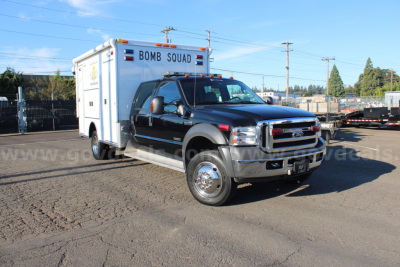 Ford F-550 cab and chassis with external box labeled BOMB SQUAD, black pickup, daytime outdoor lot.