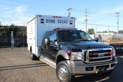 Ford F-550 cab and chassis with a rear Bomb Squad emergency box, front grille, and chrome wheels visible in a dealership lot.