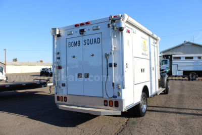 Rear view of a white Ford F-550 cab and chassis with emergency vehicle lettering and compartments.