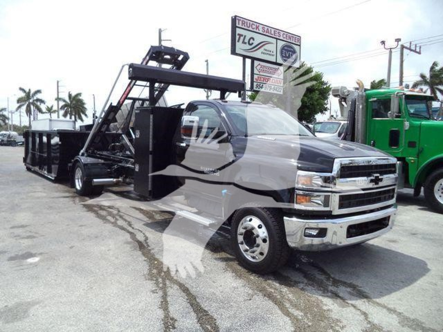 Front-left view of a new 2023 Chevrolet Silverado 6500HD truck with a heavy-duty dumping bed and hoisting mechanism, dealership lot in background.