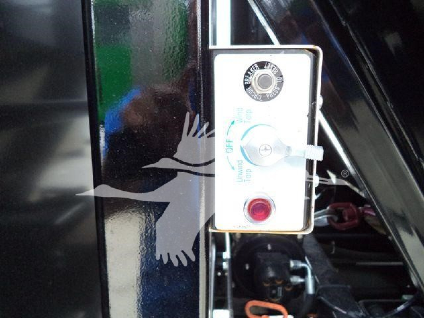 Control panel with round dial and red push button on a rectangular white switch box mounted on a black vehicle frame.