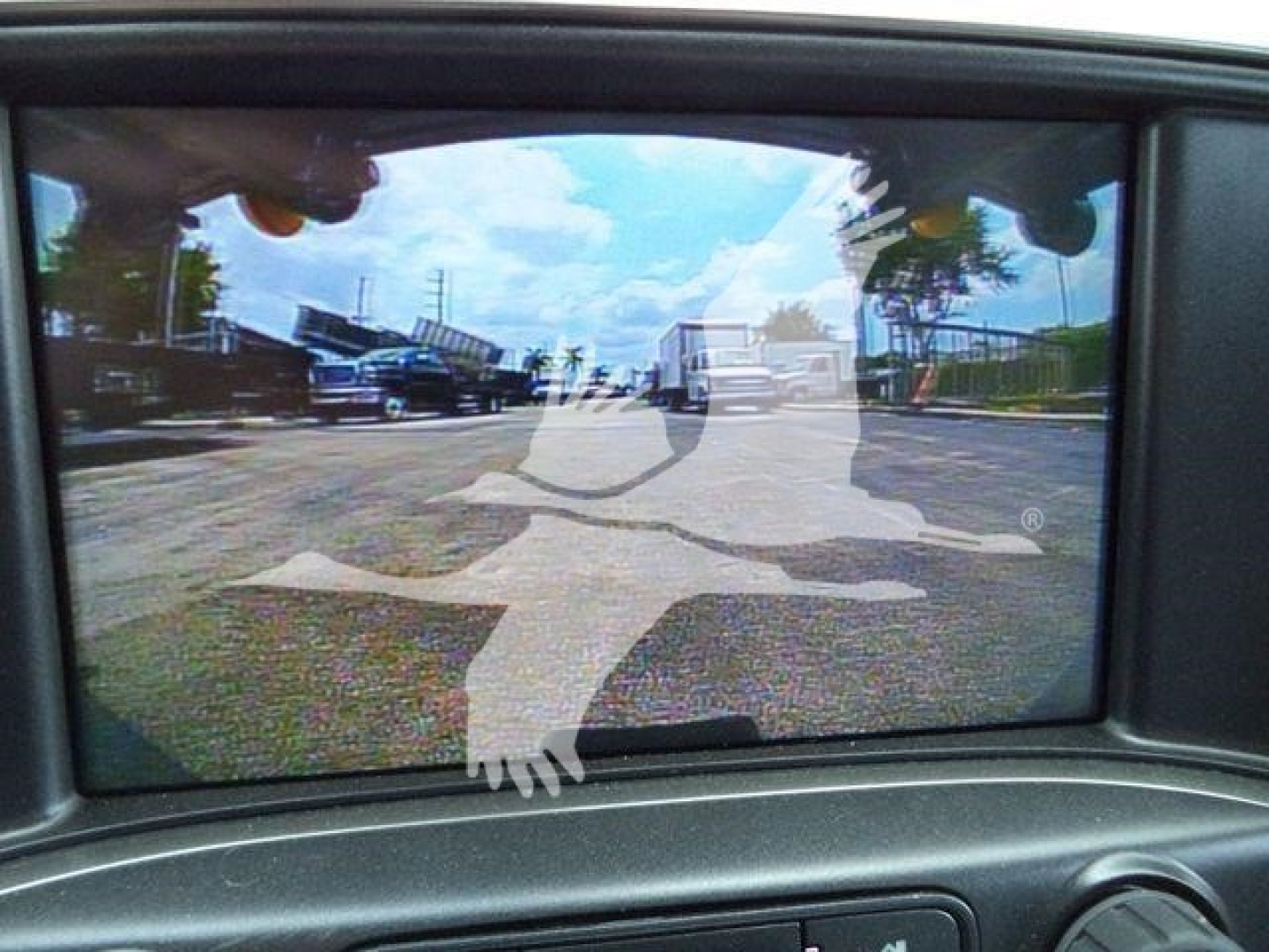 Dashboard/instrument cluster viewpoint showing rear-view mirror display with a circular road-work symbol overlay and outdoor lot reflection.