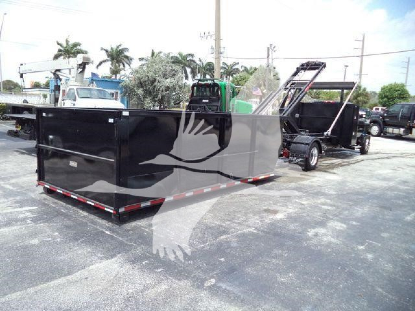 Truck trailer with black dumping bed and side railing, attached to a green vehicle in a parking lot.