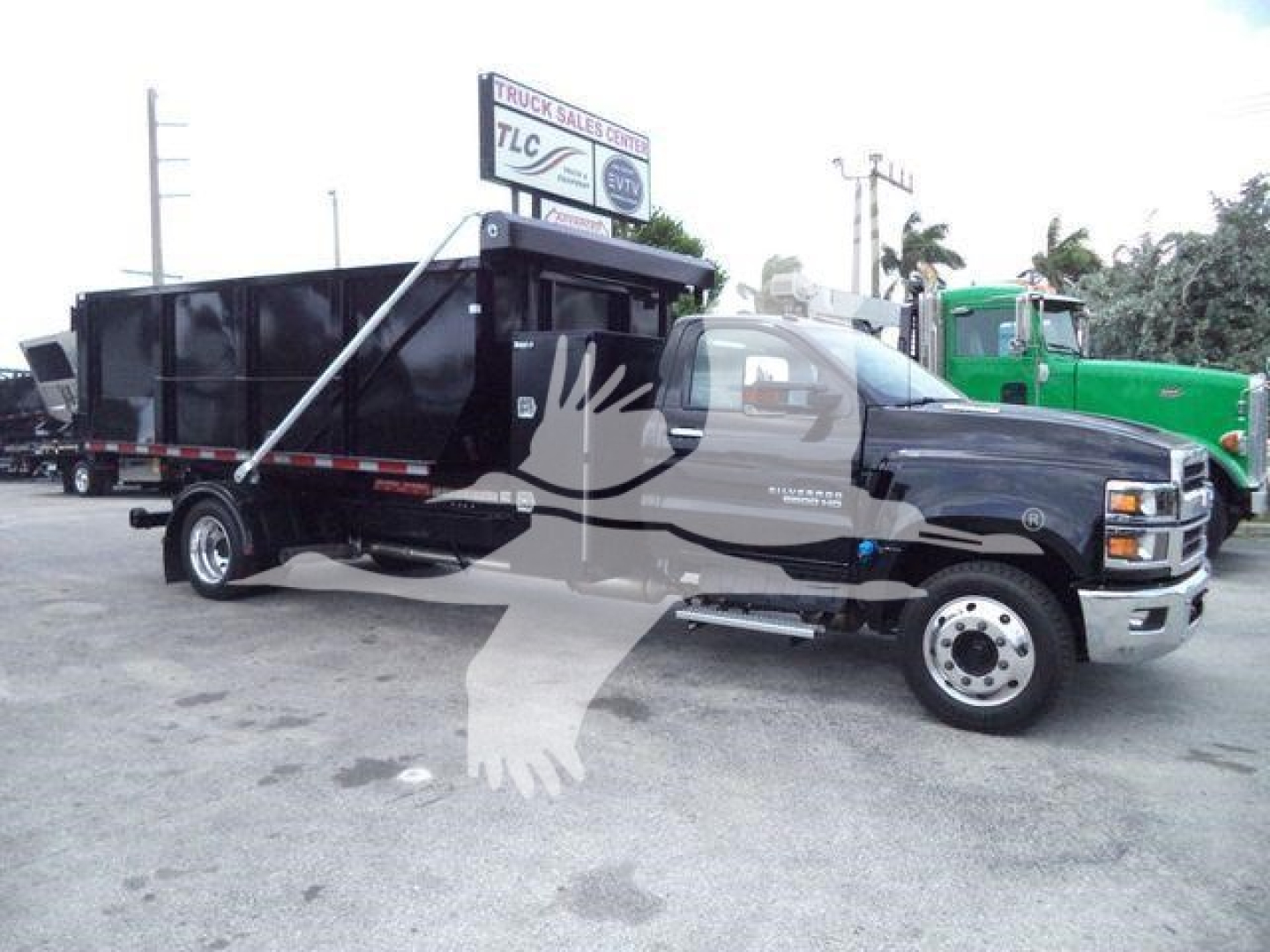 Truck bed dump body on a Chevrolet Silverado 6500HD dual rear wheels with black dump bed. Front grille shows Chevrolet emblem, side mirrors, and wheel.
