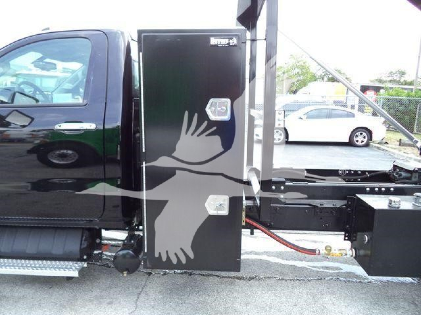 Truck cab and side storage box with two latches mounted on a flatbed trailer, black panels and hoses visible.