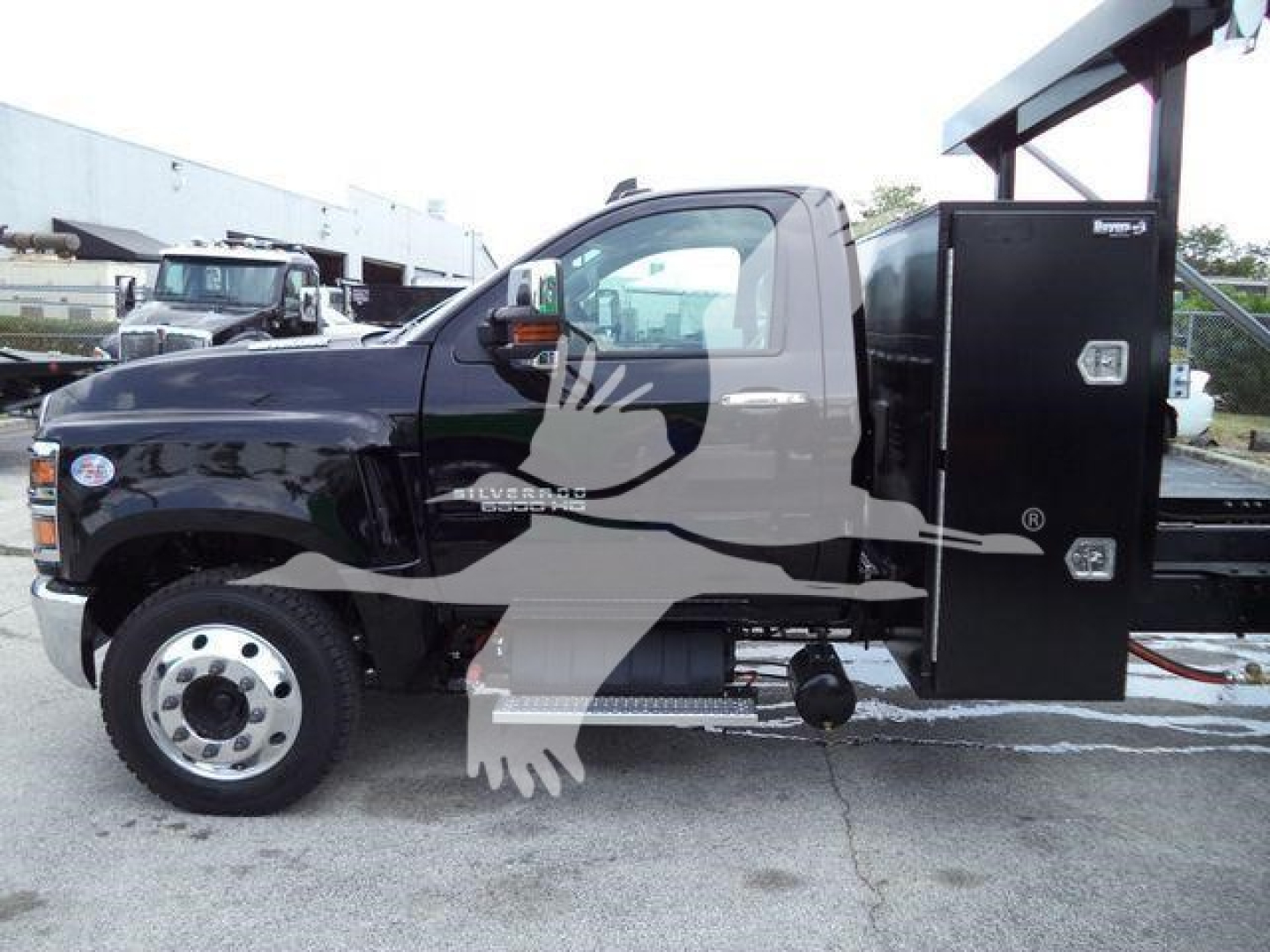 Chevrolet Silverado 6500HD cab with utility bed and crane mounting in a dealership lot; black exterior with chrome front hub, side step, and reinforced service body