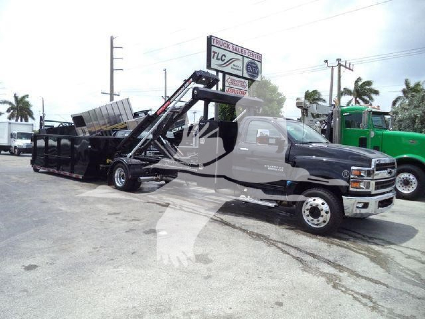 Chevrolet Silverado 6500HD truck with a hydraulic wood chip/landscape dump bed and raised tilt mechanism, front cab visible.